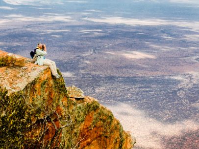Person sits on cliff looking out at Kenya with binoculars
