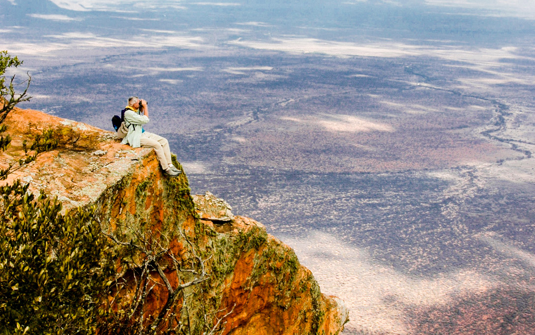 Person sits on cliff looking out at Kenya with binoculars