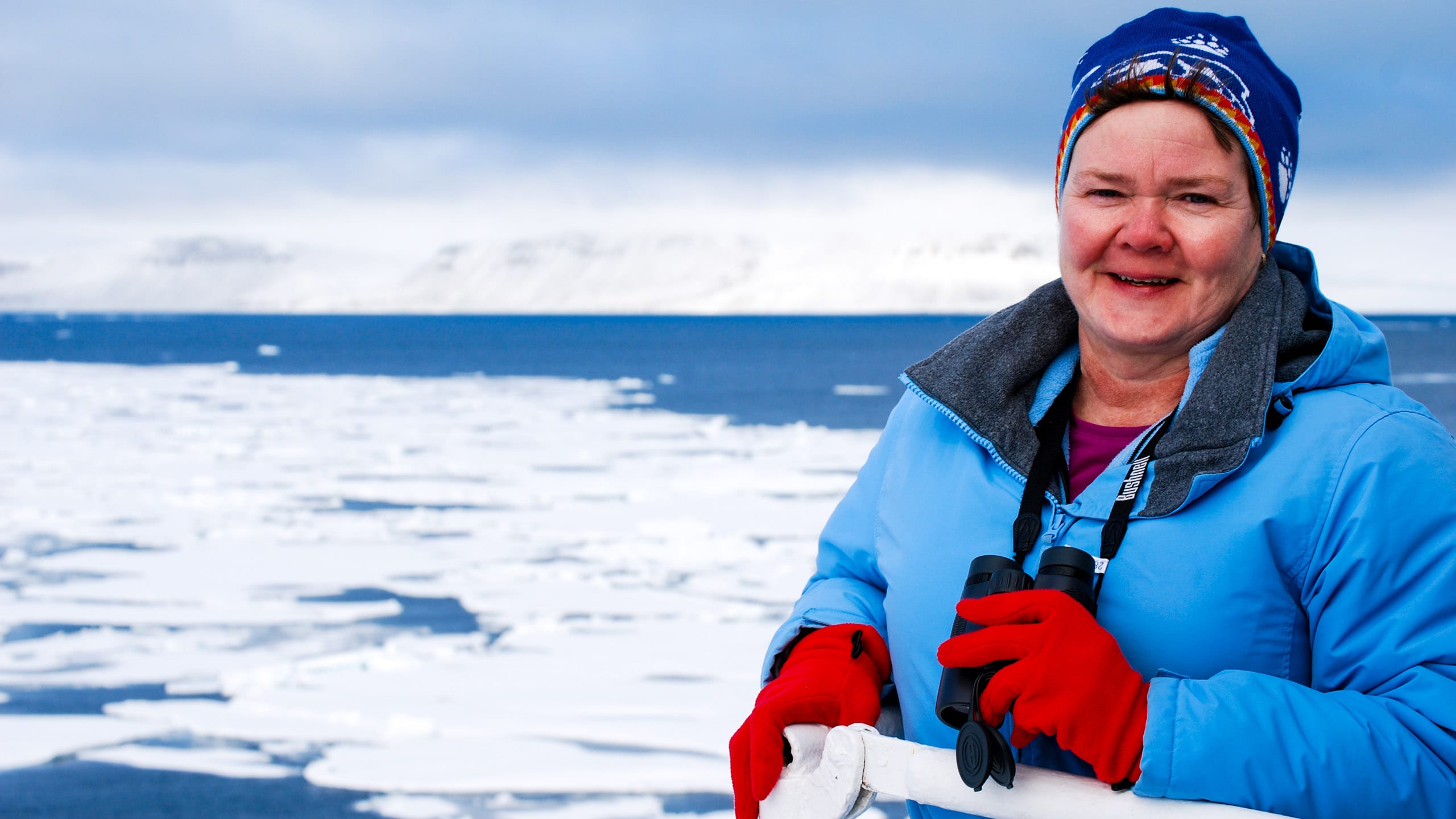 Woman stands with binoculars on arctic ship