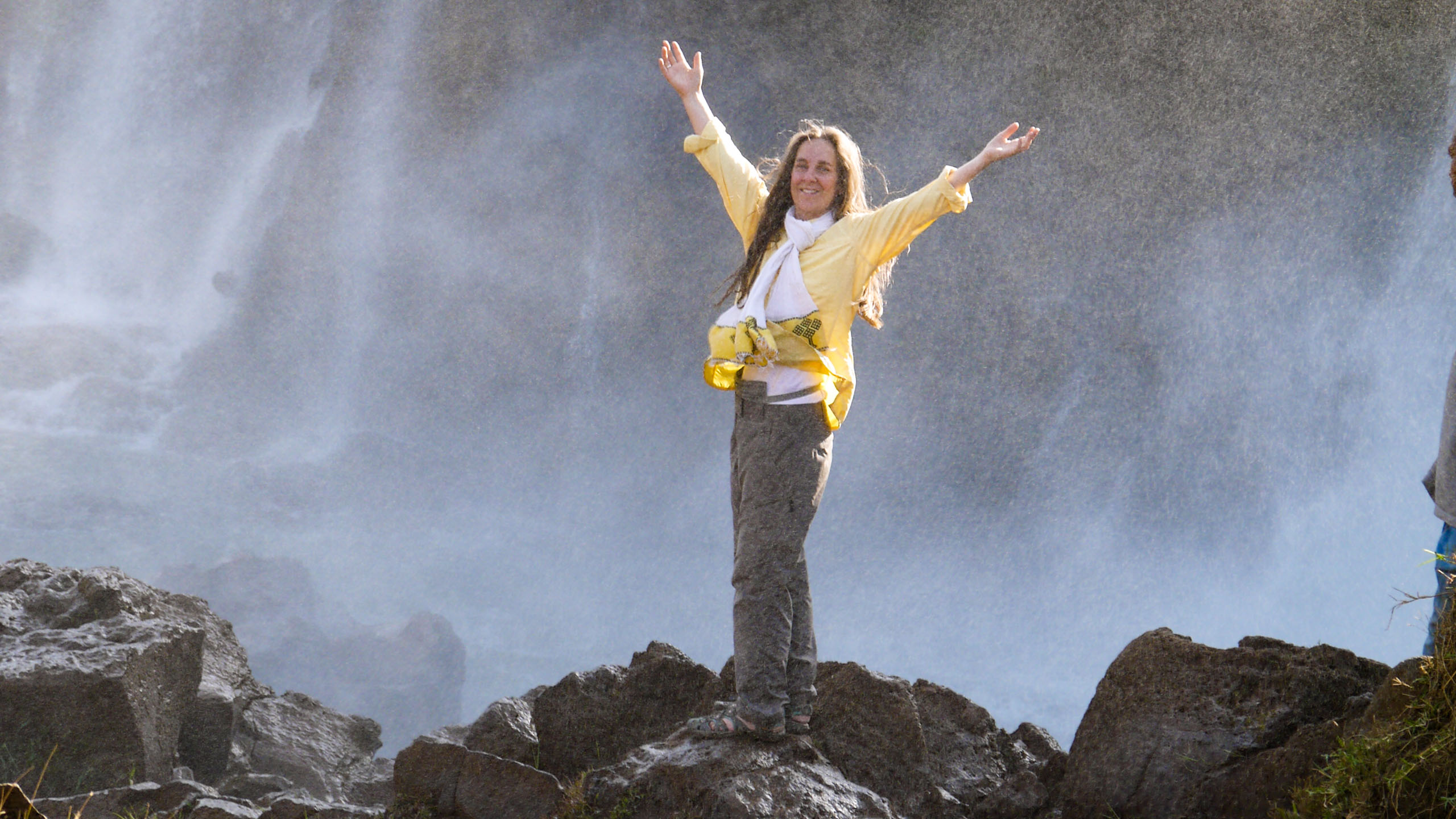 Woman holds arms up in front of Ethiopia waterfall