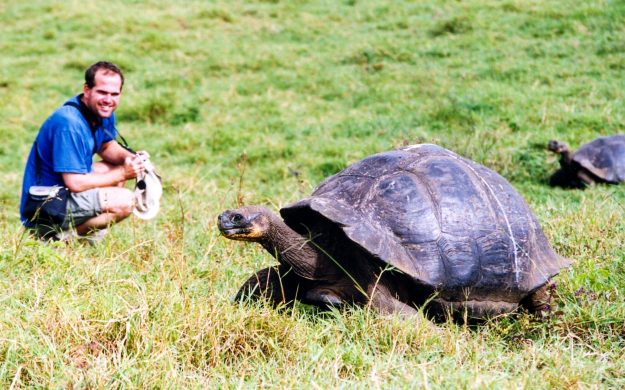 Traveler squats behind tortoise in Galapagos