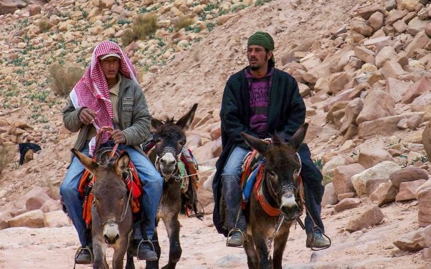 Two men ride on camels in Jordan desert