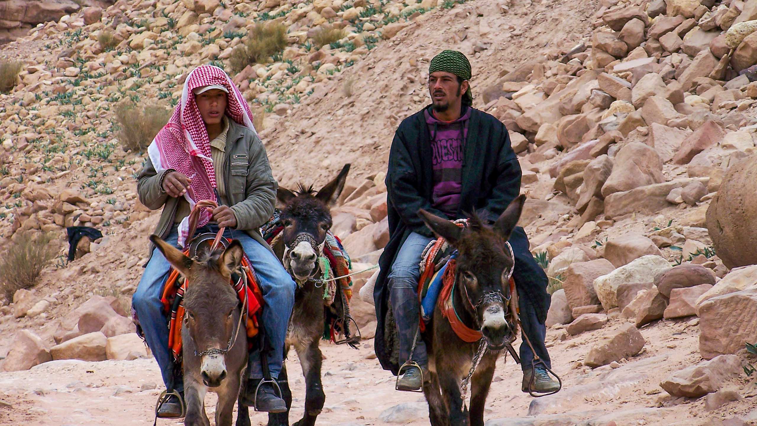 Two men ride on camels in Jordan desert