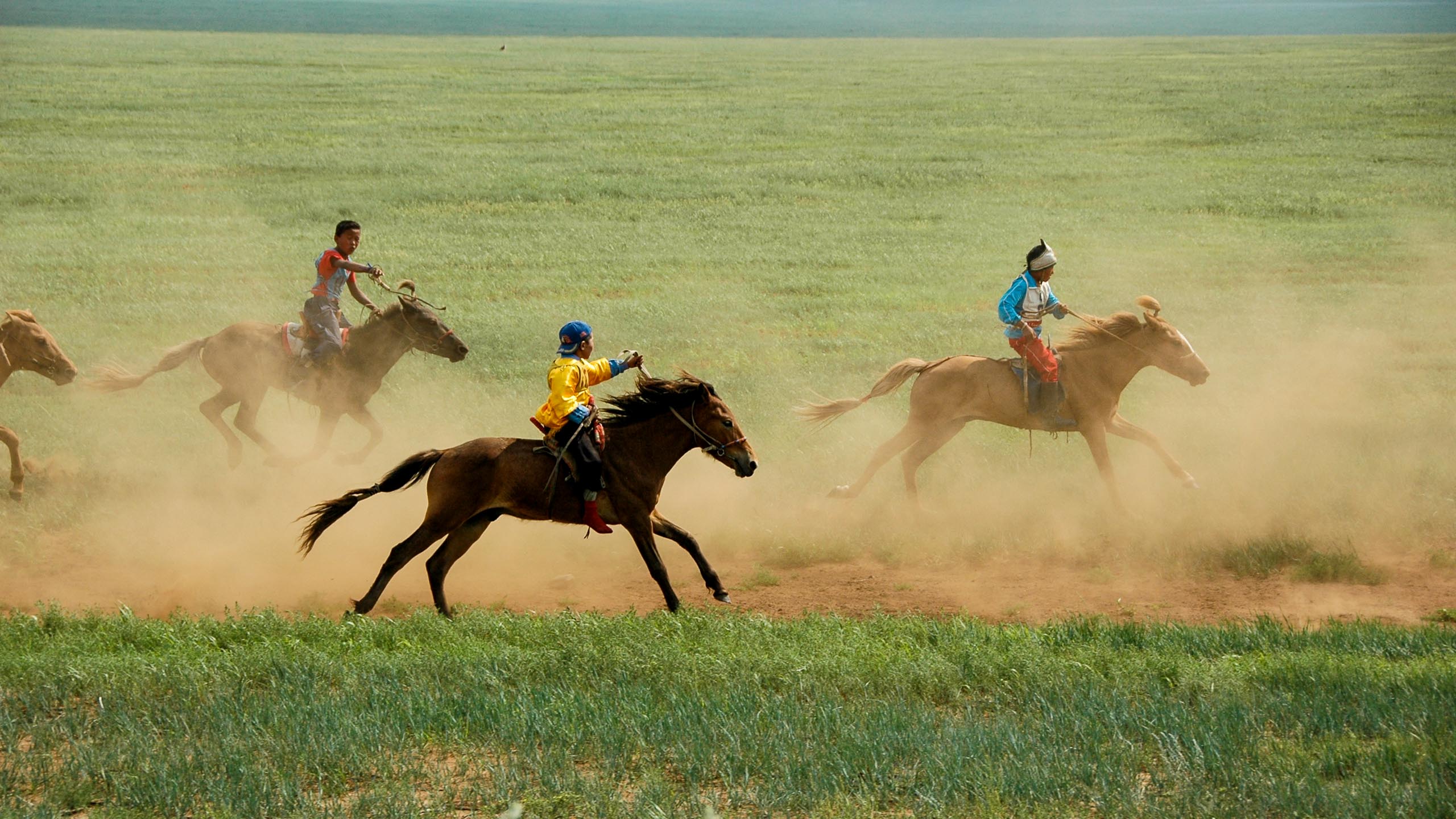 Mongolian people ride horses across plains