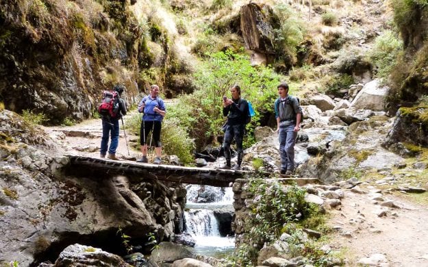 Travel group hikes across stream in Peru