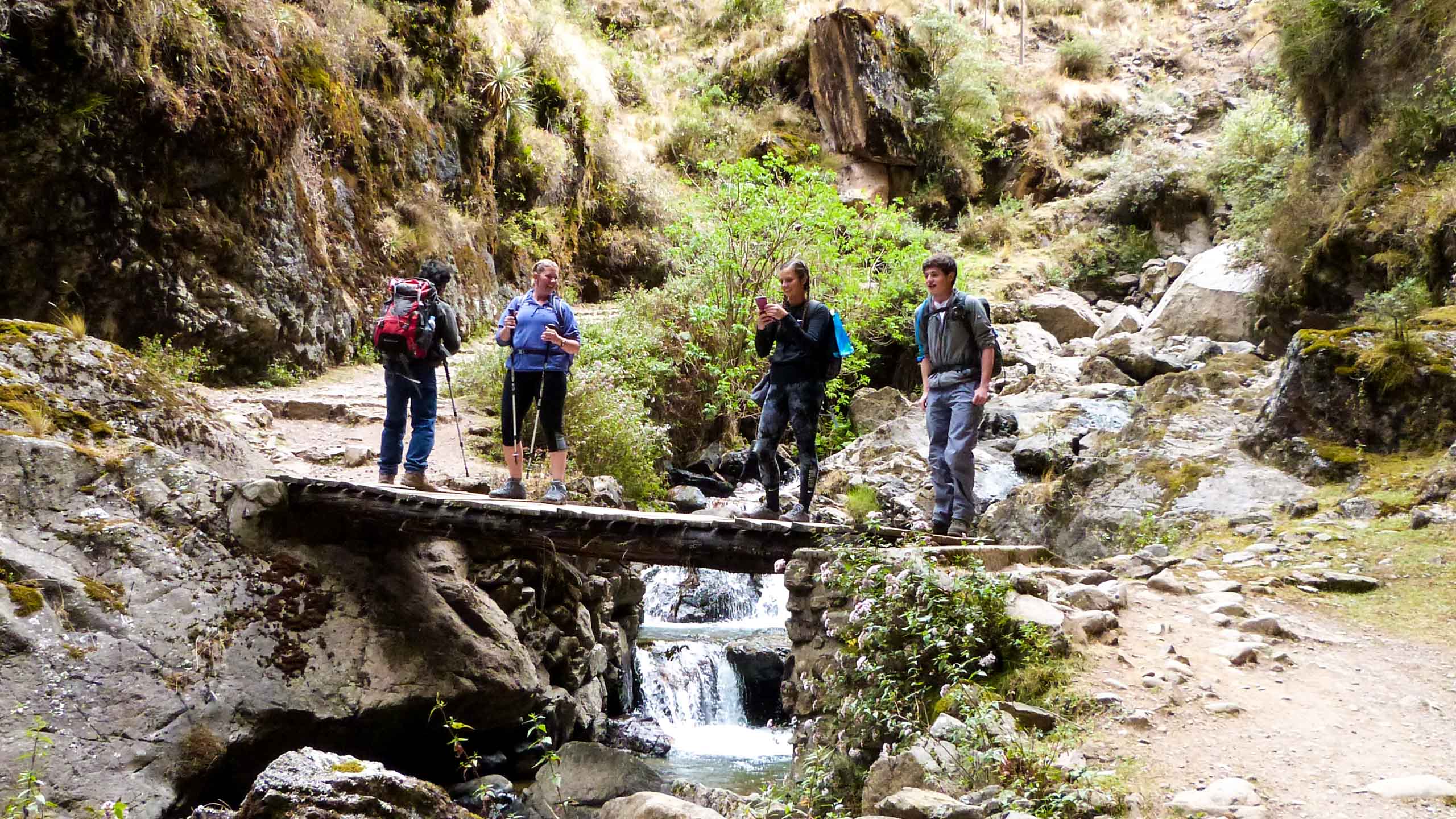 Travel group hikes across stream in Peru