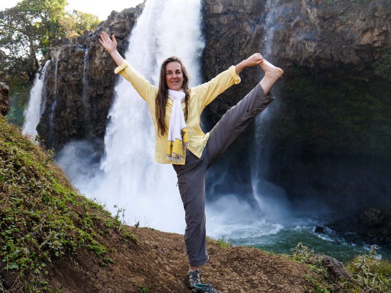 Woman does yoga pose by waterfall