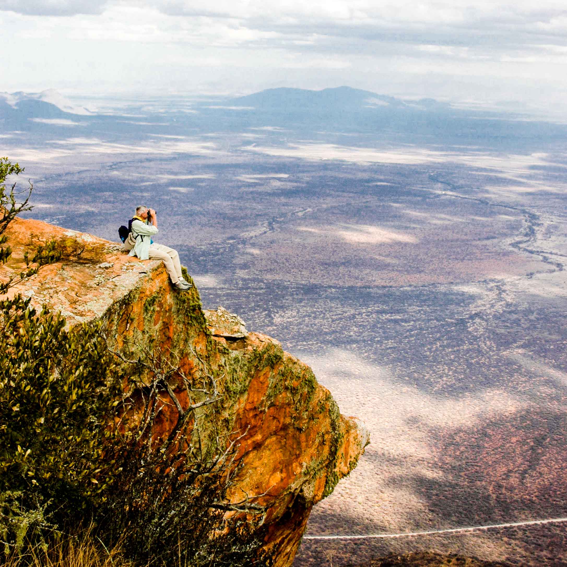 Person with binoculars sits on cliff overlooking Kenya