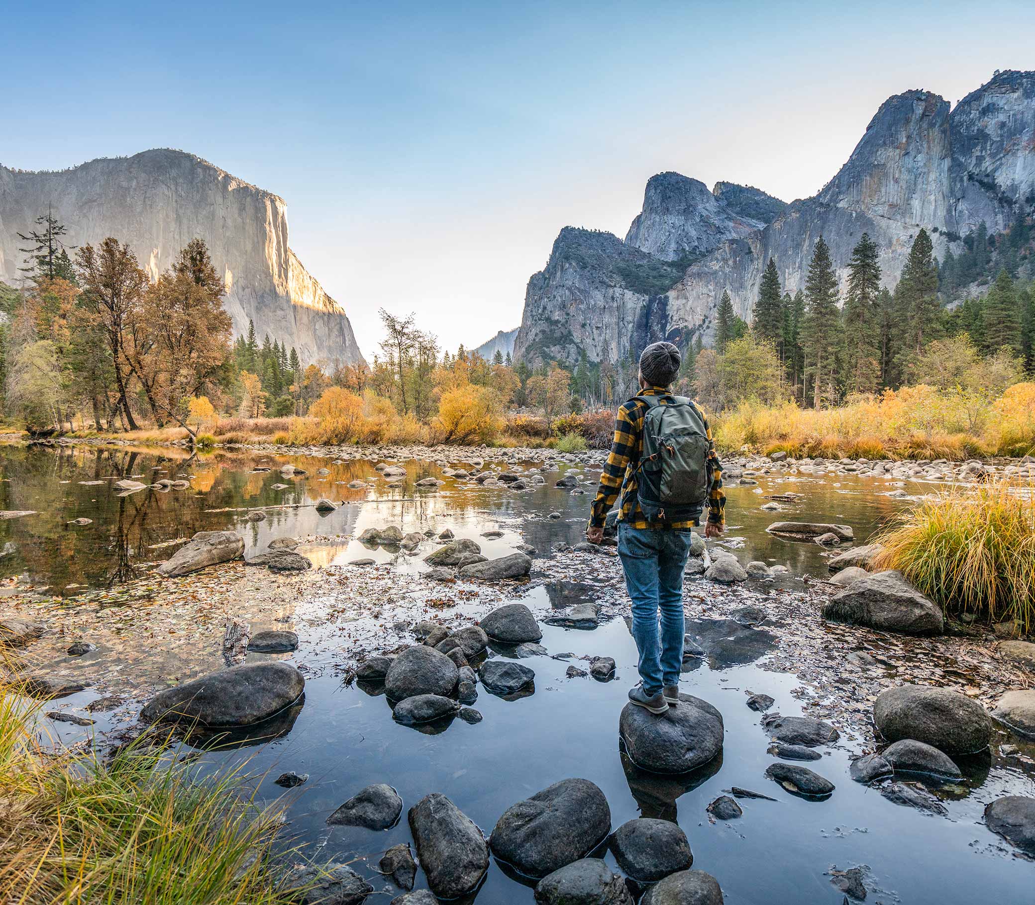 Young man contemplating Yosemite valley from the river, reflections on water surface