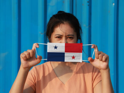 woman holding face mask shaped like Panama flag in front of face
