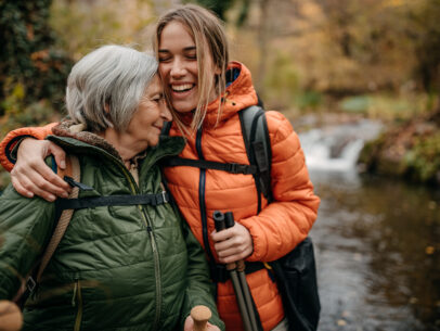 Photograph of an older woman and younger woman hugging while hiking in the woods.