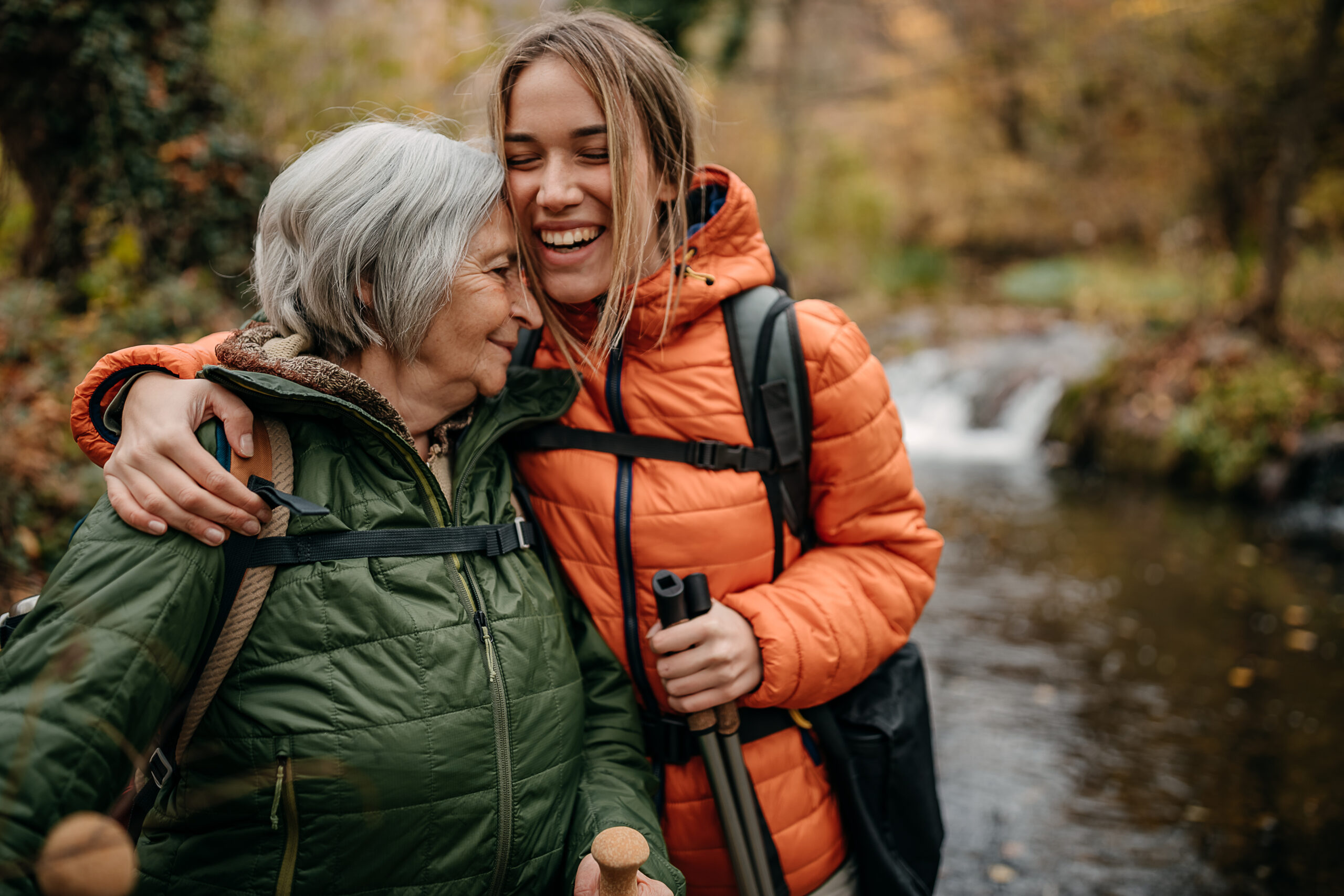 Photograph of an older woman and younger woman hugging while hiking in the woods.