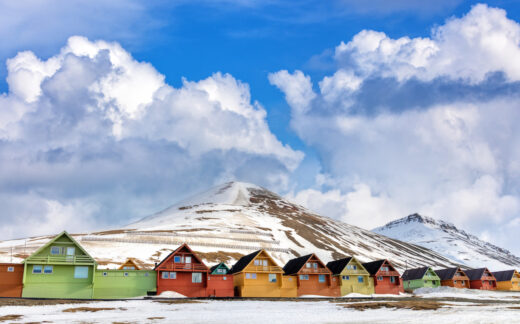 row of brightly colored houses surrounded by snow in front of mountain